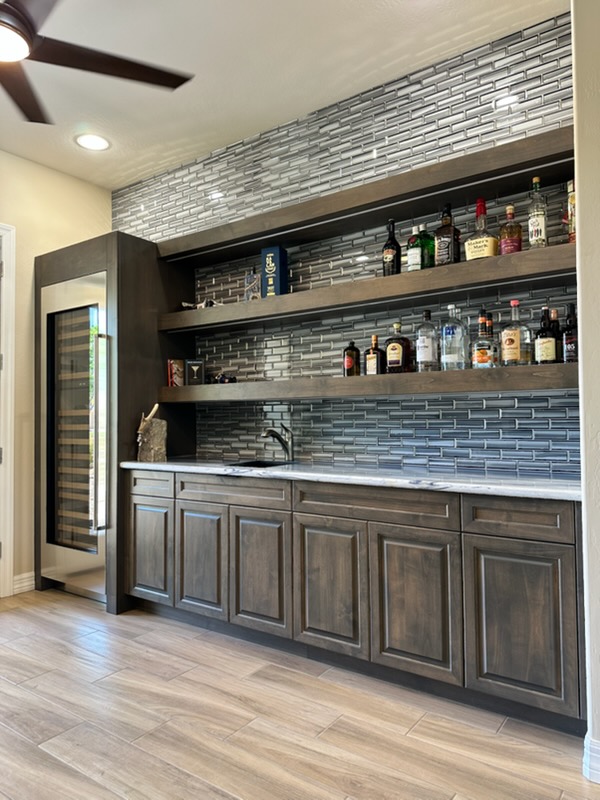 Custom home bar with wood cabinetry, floating shelves, and tile backsplash