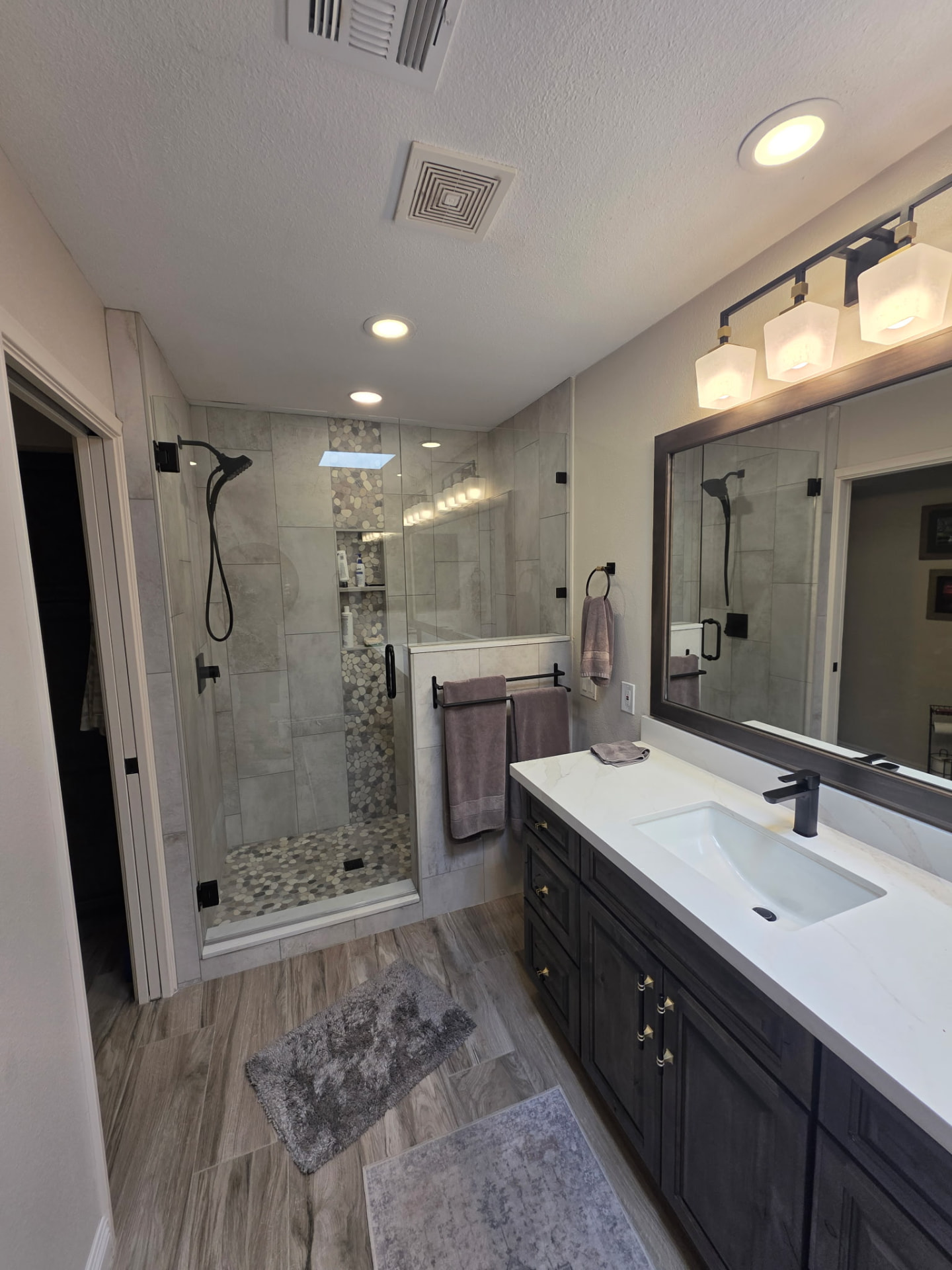 Custom tiled walk-in shower with glass door, pebble accent tile, and dark wood vanity